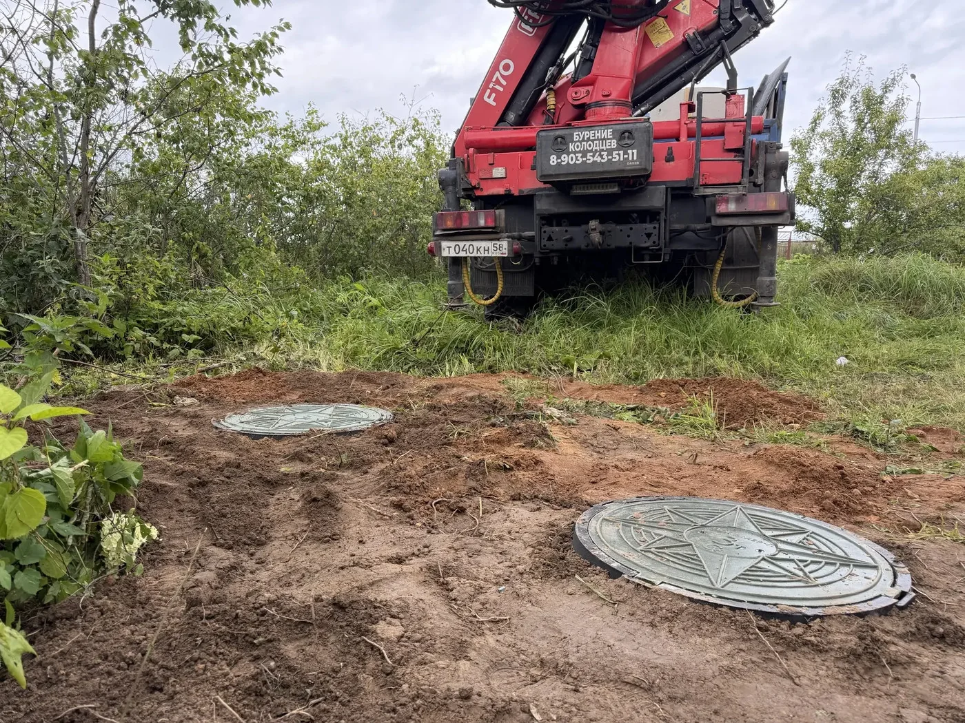 Два люка септика после засыпки грунтом, рядом манипулятор